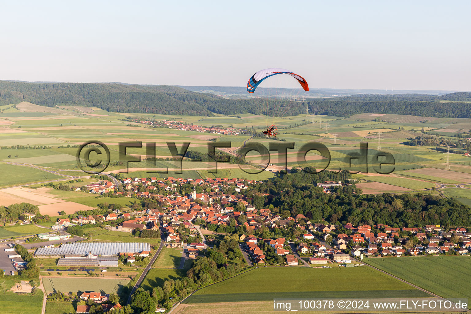 Paradlider over a Village on the edge of agricultural fields and farmland in Ruedenhausen in the state Bavaria, Germany