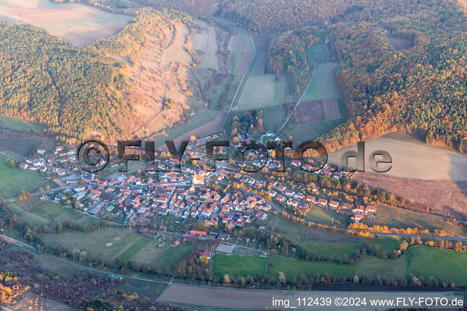 Agricultural land and field borders surround the settlement area of the village in Binsfeld in the state Bavaria, Germany from above