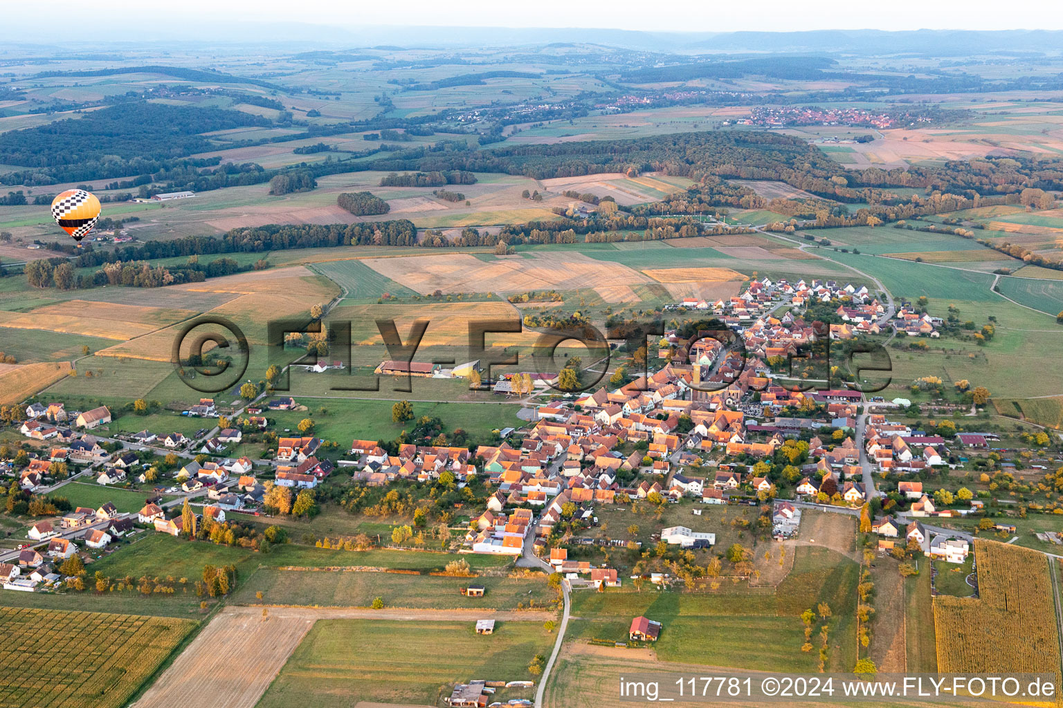 Agricultural land and field borders surround the settlement area of the village with hot air ballon in Kindwiller in Grand Est, France