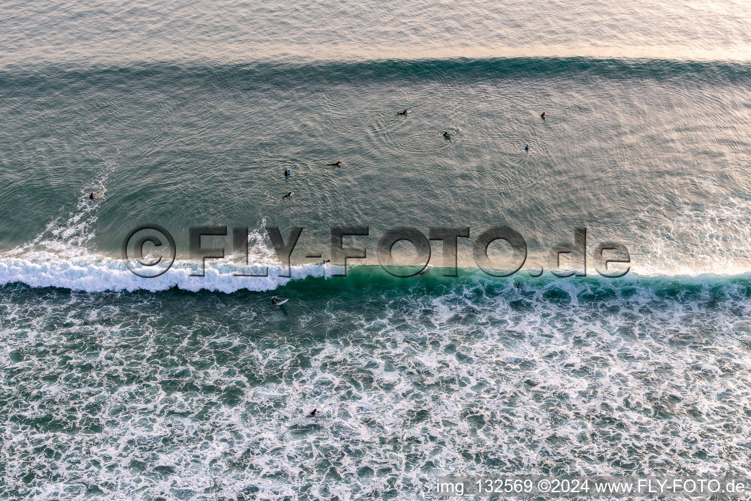 Wave surfers in front of the Plage de Tronoën in Saint-Jean-Trolimon in the state Finistere, France seen from a drone