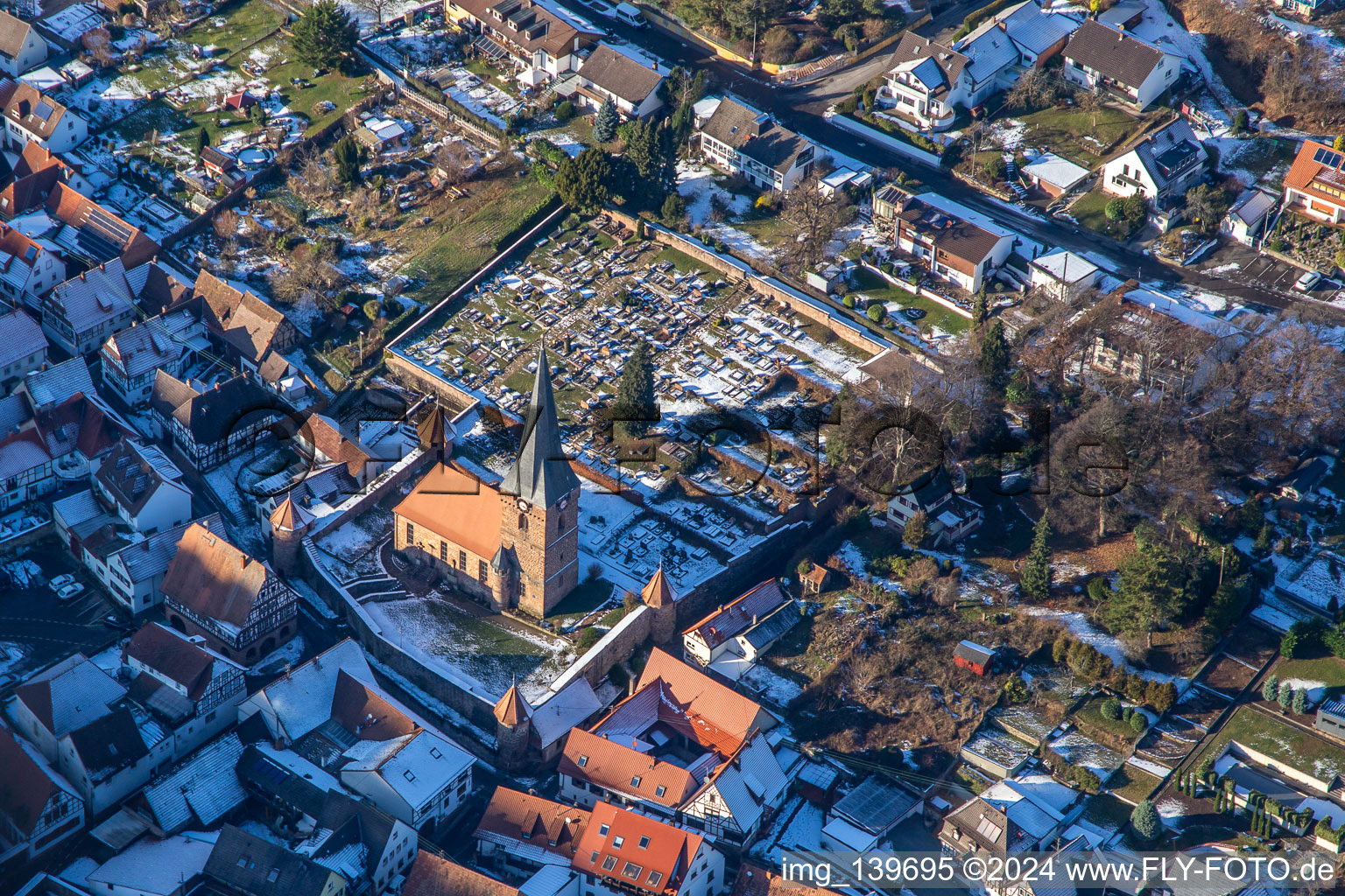 Aerial view of Fortified church of St. Martin and cemetery in winter with snow in Dörrenbach in the state Rhineland-Palatinate, Germany