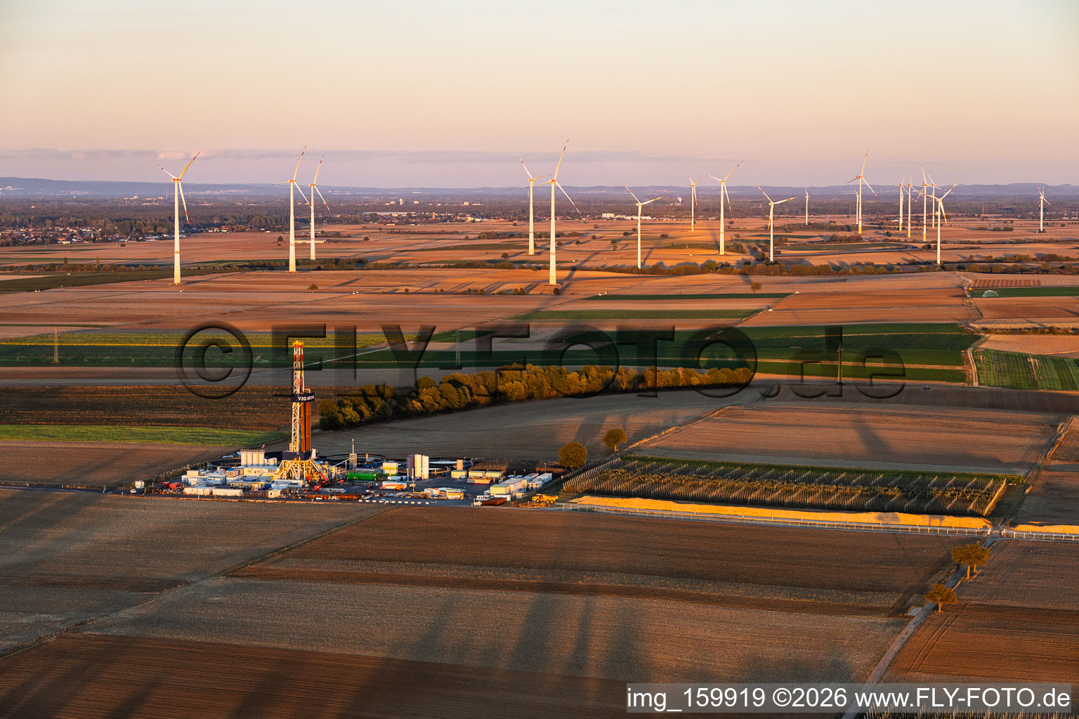 Vulcan Energy’s deep-drilling site (Rig V20 – Vercana) at Schleidberg—set against the backdrop of the Offenbach wind farm in the evening light—for the extraction of geothermal energy and lithium in Insheim in the state Rhineland-Palatinate, Germany