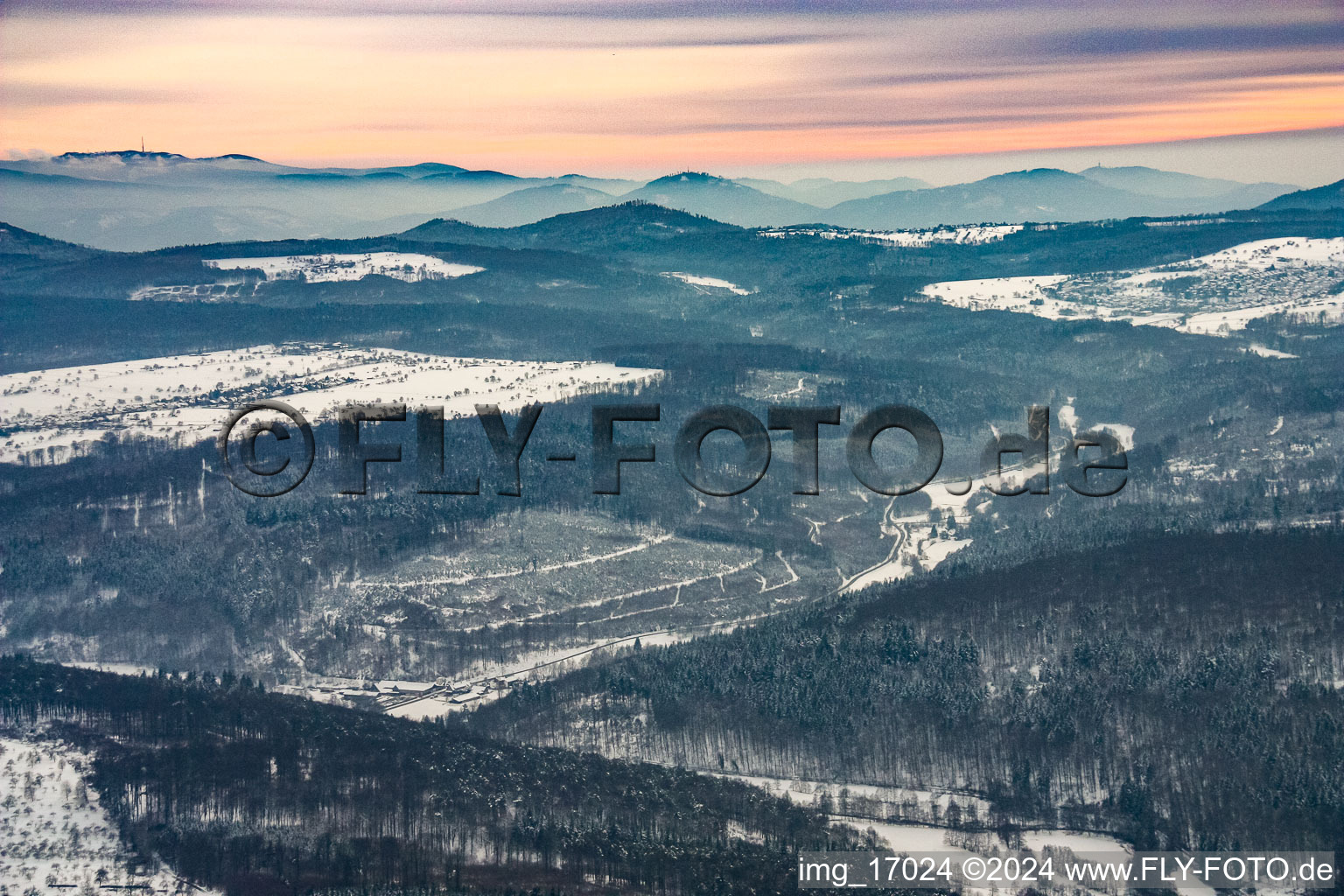 Wintry treetops in a wooded area around the snowy valley of the river Alb and panorma of the Black Forest at the horizon