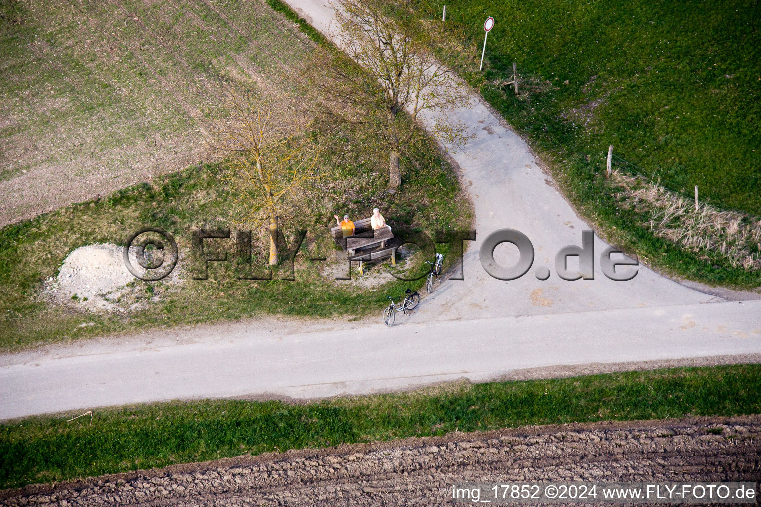 Older married couple sits on a bank on the edge of a crossroads and waves in the district of Stillern in Raisting in the federal state Bavaria