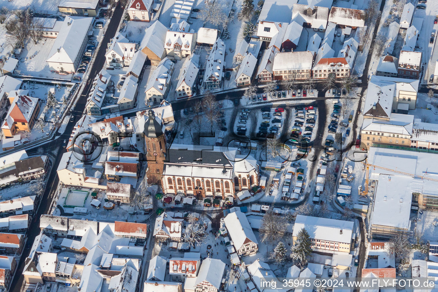 Aerial view of Wintry snowy Christmassy market event grounds and sale huts and booths on market place around tha church Sankt Georgskirche in Kandel in the state Rhineland-Palatinate, Germany