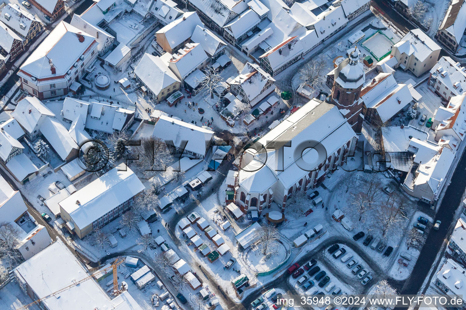 Aerial view of Wintry snowy Christmassy market event grounds and sale huts and booths on market place around tha church Sankt Georgskirche in Kandel in the state Rhineland-Palatinate, Germany