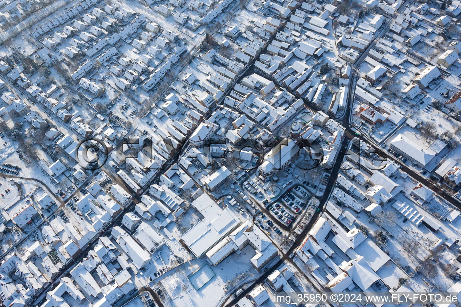 Aerial view of Wintry snowy Christmassy market event grounds and sale huts and booths on market place around tha church Sankt Georgskirche in Kandel in the state Rhineland-Palatinate, Germany