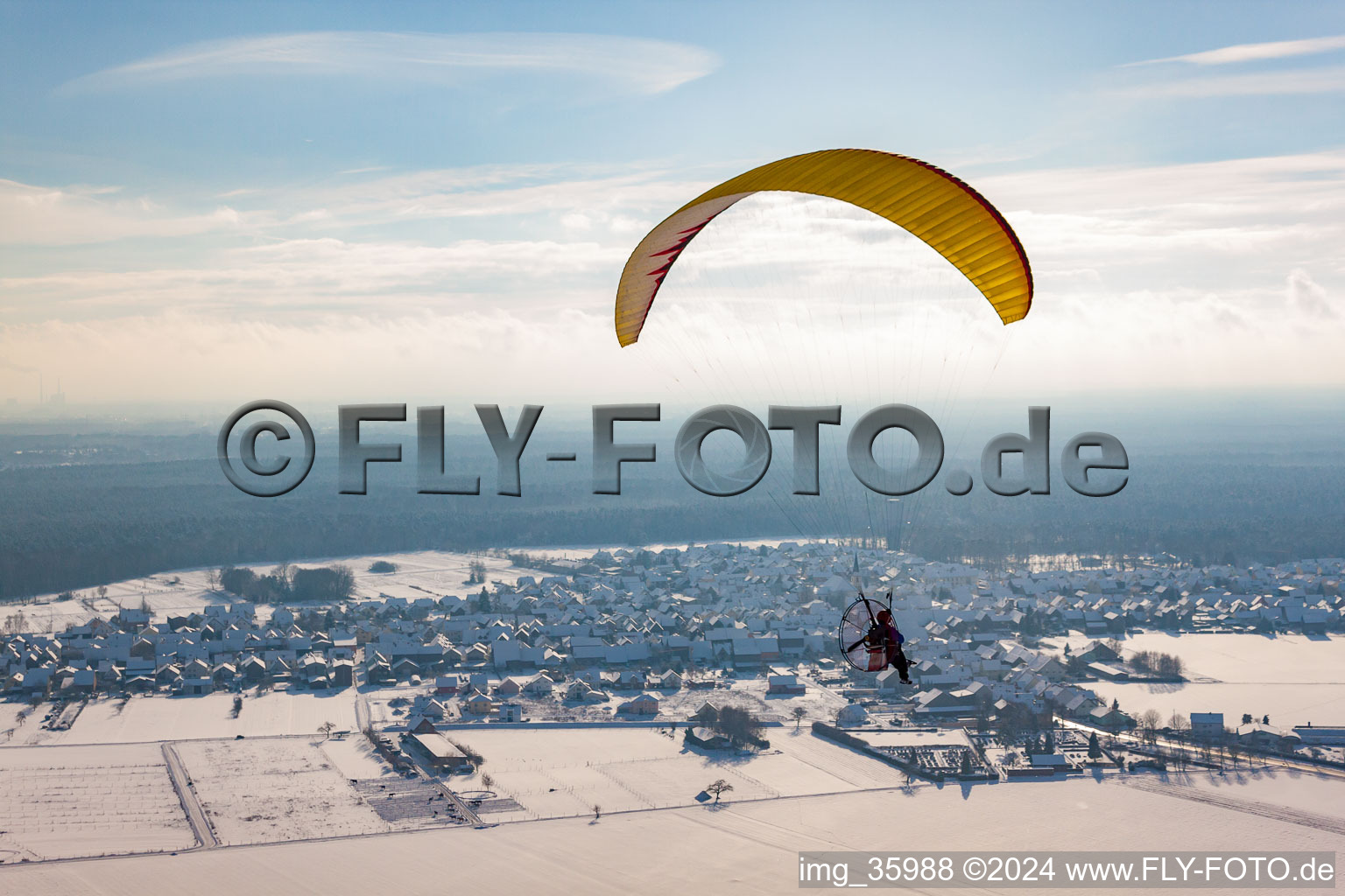 Powered paraglider flying over winterly snow-covered village in Hatzenbuehl in the state Rhineland-Palatinate