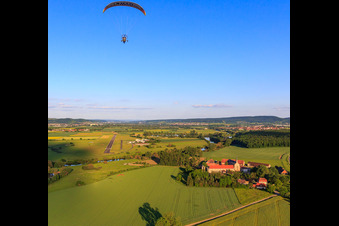 Paraglider over the estate Mariaburghausen with the Church of St. John the Baptist Mariaburghausen in the district Mariaburghausen in Haßfurt in the state Bavaria, Germany