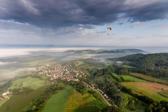 Paraglider before the Lake of Constance hidden by mroning fog over Village - view on the edge of agricultural fields and farmland in the district Guettingen in Radolfzell am Bodensee in the state Baden-Wurttemberg, Germany