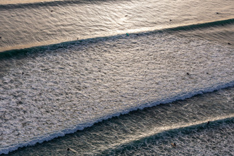 Wave surfers in front of the Plage de Tronoën in Saint-Jean-Trolimon in the state Finistere, France from the drone perspective