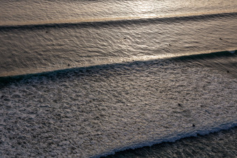 Wave surfers in front of the Plage de Tronoën in Saint-Jean-Trolimon in the state Finistere, France from a drone