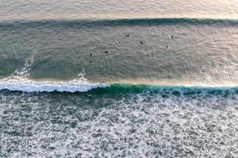 Wave surfers in front of the Plage de Tronoën in Saint-Jean-Trolimon in the state Finistere, France seen from a drone