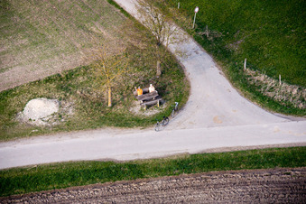Older married couple sits on a bank on the edge of a crossroads and waves in the district of Stillern in Raisting in the federal state Bavaria