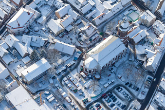 Aerial view of Wintry snowy Christmassy market event grounds and sale huts and booths on market place around tha church Sankt Georgskirche in Kandel in the state Rhineland-Palatinate, Germany