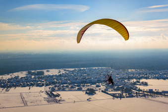 Powered paraglider flying over winterly snow-covered village in Hatzenbuehl in the state Rhineland-Palatinate