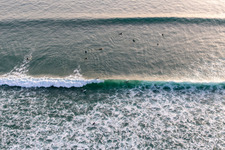 Wave surfers in front of the Plage de Tronoën in Saint-Jean-Trolimon in the state Finistere, France seen from a drone